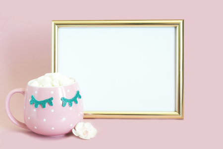 a mock up golden photo frame and next to it is a pink polka dot mug with coffee and marshmallows...