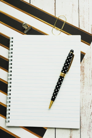 Notebook on a spring, a pen and a clip in the form of a heart on a striped paper and gray wooden...