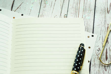 A black pen with polka dots, an open notebook, paper with black and gold peas, a paper clip and shiny little stars. Space for text.の写真素材