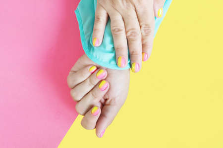 Female hands in a blue blouse with a bright pink-yellow manicure on a yellow-pink background.の写真素材
