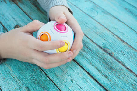 The child is busy with a puzzle in the form of a ball with colorful balls inside on a blue wooden background.の写真素材