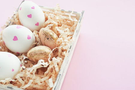 Easter white eggs with pink hearts and beige in black speck and gold strokes in a basket on a pink...
