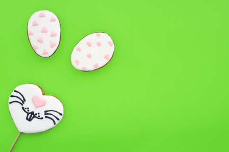 Gingerbread in the shape of a heart with a painted rabbit face and gingerbread cookies in the shape of eggs on a green background. Space for text. Easter bunny.の写真素材