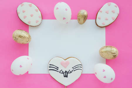 Gingerbread eggs with painted hearts and in the shape of hearts with a painted muzzle of a hare and eggs with painted hearts and gold on a pink background. White rectangle in the middle.の写真素材