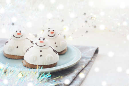 three cakes in the form of a snowman on a blue plate, a linen towel, garlands and tinsel. Lights bokeh. space for copy.の写真素材