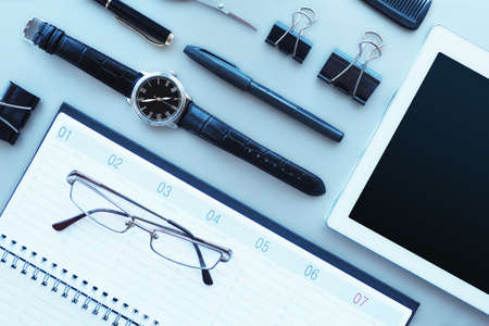 Gray desktop with a glider, tablet, glasses, clock, pens, scissors, clamps. Top view, flat layout.の写真素材