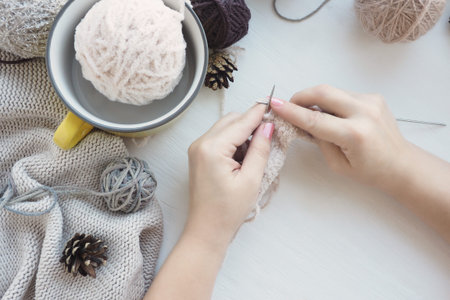 women's hands on a white table knit with plush yarn lying in a yellow ceramic cup, knitted beige...