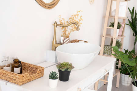 bright bathroom, sink, mixer, mirror, wicker basket and flowers on a white cabinet.の写真素材