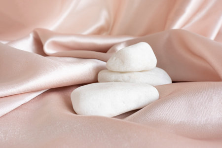 three white quartz stones on a pink satin background with folds. Luxurious showcase for advertising...