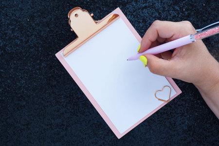 female hands with bright yellow manicure pen writes on a clipboard. shiny black background.