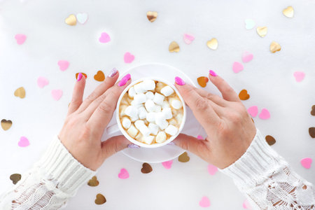 female hands with beautiful manicure hold a cup with coffee and marshmallows on a white background...