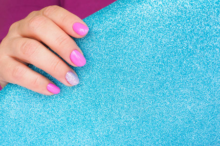 female hands with beautiful lilac manicure hold shiny blue paper with glitter. space for text.