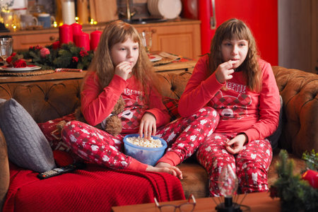 two teenage girls with loose hair in red pajamas are watching a movie and eating popcorn.