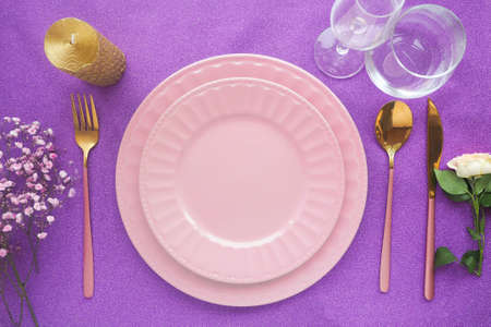 two empty ceramic plates on a shiny purple background, stylish cutlery rose and gold cutlery, a candle and glasses.の写真素材