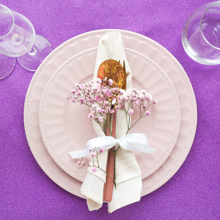 set table: gypsophila flower, napkin and cutlery on ceramic plates on a shiny purple background.
