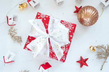 red gift box with a white bow, Christmas balls and garland houses on a white background.