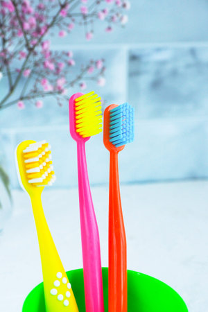 three bright multi-colored toothbrushes in a green cup and pink gypsophila flowers.