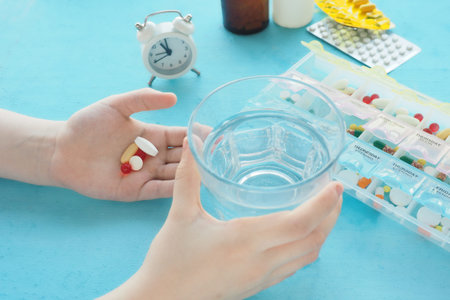 child's hands are holding a glass of water and pills, a container with pills and an alarm clock.