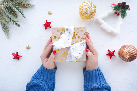 female hands in a blue sweater hold a box with a Christmas present, stars and Christmas balls on a...