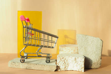a grocery cart on a concrete slab, concrete podiums and yellow plexiglass on a beige background.の写真素材