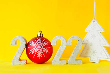 Celebrating the new year 2022. Number 2022 with concrete numbers and a Christmas tree ball on a yellow background with a Christmas tree figurine.の写真素材