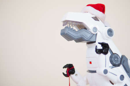 toy robot dinosaur in a santa hat and with a fir ball on a beige background. copy space.の写真素材