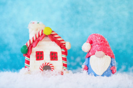 Christmas card figurine of a funny gnome and a gingerbread house in the snow on a blue background.の写真素材