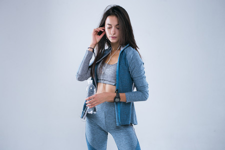 Beautiful fitness woman posed with bottle of water in earphones. Girl touch earphones and smile.の写真素材