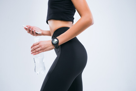 The body of fitness and slim young woman with bottle of water and mobile phone in her hands. Sport clock on woman's hand.の写真素材