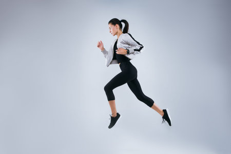 Vertical image of sports woman running over gray background. Fitness young woman doing morning...