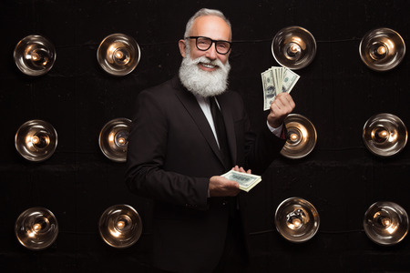 Happy bearded man carry carrying many banknote of dollars and smile, wearing in formal wear and fashion glasses. Looking in the camera. Happy of money prize.の写真素材
