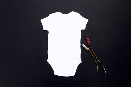 Blank white baby bodysuit on a black background with wild flowers to the left