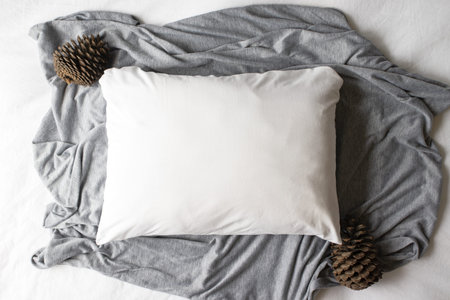 Plain white pillowcase on a grey and white textile background with pine cones - winter Christmas...