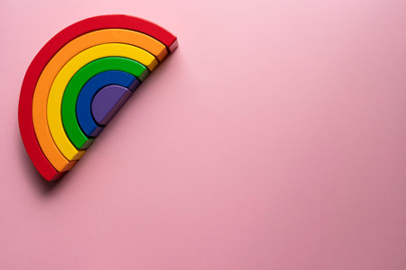 Wooden rainbow toy top left on a pink background - creative flat lay montessori composition