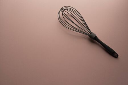 Single grey whisk at the top right of a plain pastel pink background - kitchen utensil minimal compositionの写真素材