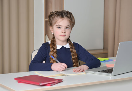 European school girl with pigtails and school uniform looking at camera, holding pen and taking notes in exercise book. Back to school, learning and education concept.の写真素材