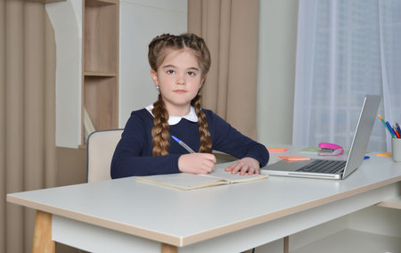 Cute school girl with pigtails and uniform looking at camera, taking notes or writing in exercise book. Back to school, learning and online education concept.の写真素材