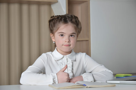 Back to school and education concept. Cute little girl in school uniform showing thumbs up sign and looking at camera. Child from elementary school sitting at desk.の素材 [FY310189456622]