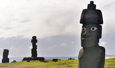 Three Moai statues (Ahu Tongariki) against a cloudy sky, green grass and ocean, Easter Island (Rapa Nui), Chile. One of the most famous and beautiful attractions in Latin America.の写真素材