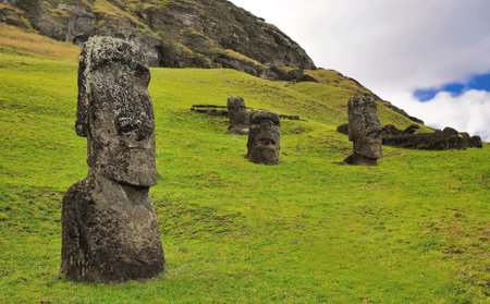 Moai statues against a blue sky with clouds and green grass field in the Rano Raraku Volcano in Easter Island, Rapa Nui National Park (Chile)の写真素材