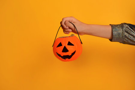 Halloween pumpkin candy bucket with sweets in female child hand on yellow background with copy space.の写真素材