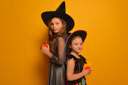 Sisters girls in witches costumes with ignited candles or burning candles and looking at camera on yellow background.の写真素材