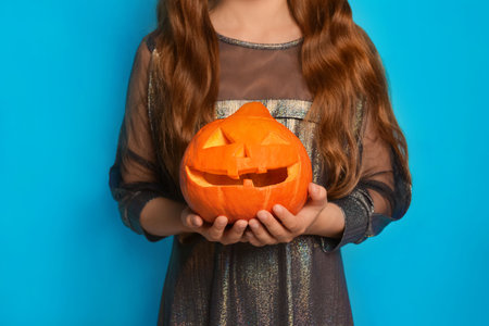 Close-up of a orange Halloween carved pumpkin or Jack o lantern pumpkin in female hands on a blue background. Unrecognizable child girl holding pumpkin in hands.の写真素材