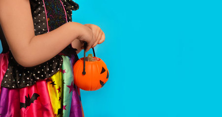 Child girl's hands holding orange pumpkin candy basket or Halloween Jack o Lantern candy bucket with sweets on a blue background with copy space. Trick or treat concept.の写真素材