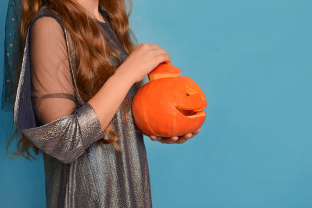 Halloween pumpkin or Jack o lantern pumpkin in female hands on a blue background. Unrecognizable child girl holding carved pumpkin, main symbol of Halloween Day, in hands.の写真素材