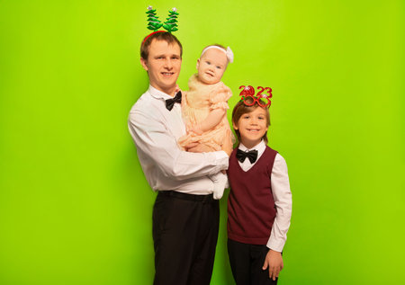 Happy smiling cheerful family father, daughter and son wearing costumes and dress, party glasses and looking at camera on green background. New Year 2023 or Christmas celebration.の写真素材