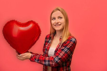 Excited dreaming happy girl holding red heart shaped air balloon, wearing checkered plaid shirt and looking up isolated on pink background. St Valentines Day and love concept.の写真素材