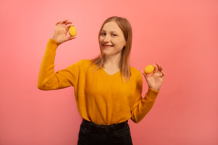 Happy smiling positive girl in yellow sweater with black jeans holding two yellow painted easter eggs or two dyed easter eggs and looking at camera isolated on pink background.の写真素材