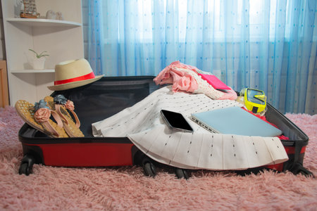 Preparation and packing things for holidays vacations: open red suitcase with laptop, mobile phone, summer clothes, swimming mask, straw hat, slippers and passport with money.の写真素材