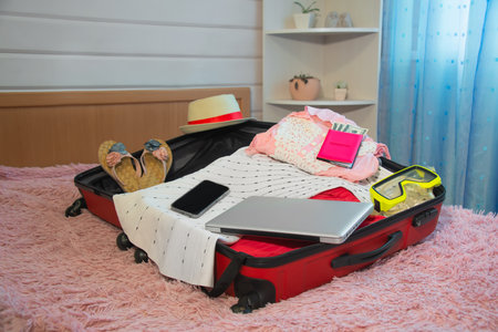 Packing suitcase for traveling or preparation travel case bag of silver laptop, mobile phone, female summer clothes, swimming mask, straw hat, slippers and passport with money.の写真素材